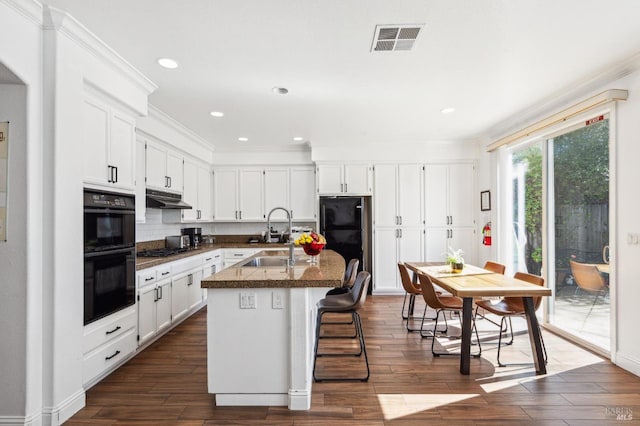 kitchen with tasteful backsplash, visible vents, white cabinetry, an island with sink, and black appliances