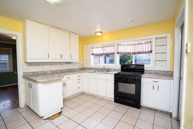 kitchen featuring tasteful backsplash, light countertops, white cabinetry, black gas stove, and a sink