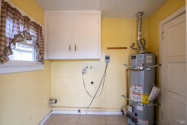 clothes washing area featuring cabinet space, secured water heater, light tile patterned floors, and baseboards