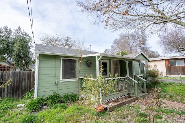view of front of home featuring roof with shingles, covered porch, and fence