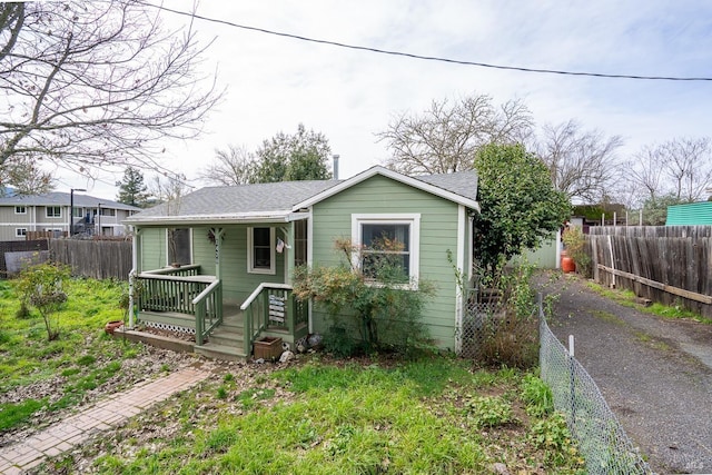 bungalow-style home with fence private yard, covered porch, and roof with shingles