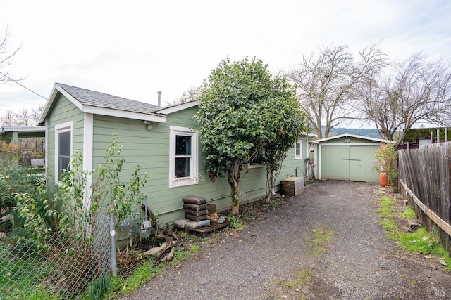 exterior space with a shed, a detached garage, aphalt driveway, fence, and an outbuilding