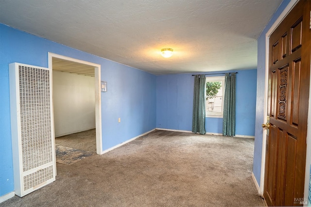 carpeted empty room featuring baseboards, a heating unit, and a textured ceiling