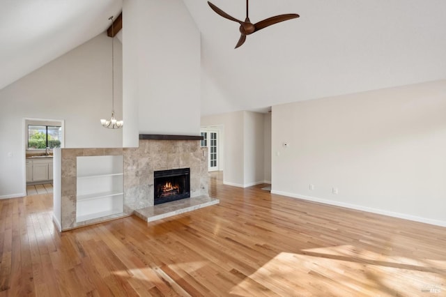 unfurnished living room with baseboards, a tiled fireplace, light wood-type flooring, a sink, and ceiling fan with notable chandelier