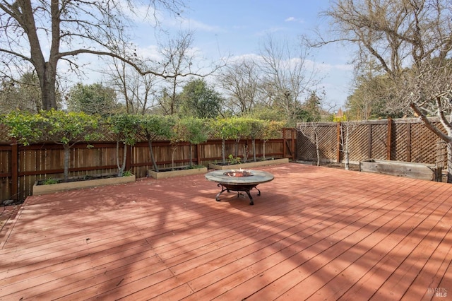 wooden deck with a fenced backyard and a fire pit