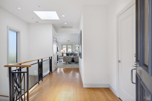 hallway featuring a skylight, light wood finished floors, baseboards, visible vents, and recessed lighting