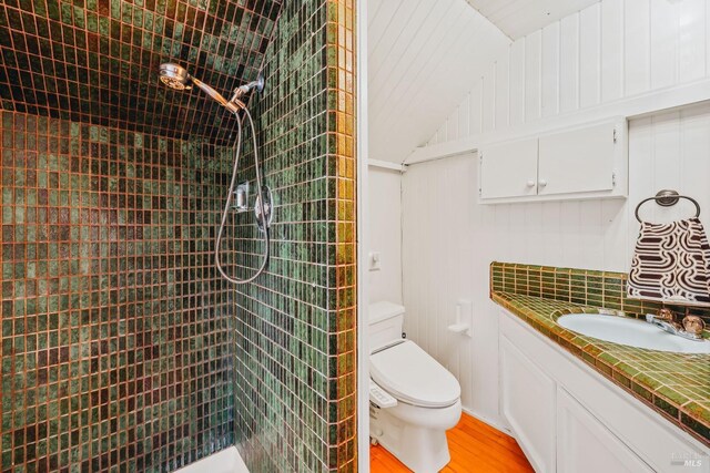 bathroom with vaulted ceiling, a tile shower, toilet, and wood finished floors