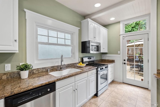 kitchen with a wainscoted wall, appliances with stainless steel finishes, white cabinetry, a sink, and dark stone counters