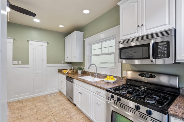 kitchen featuring dark stone counters, a wainscoted wall, appliances with stainless steel finishes, white cabinetry, and a sink
