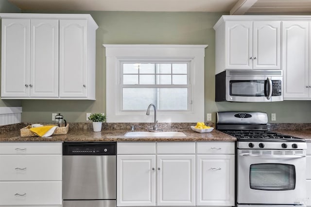 kitchen featuring dark stone counters, appliances with stainless steel finishes, a sink, and white cabinets