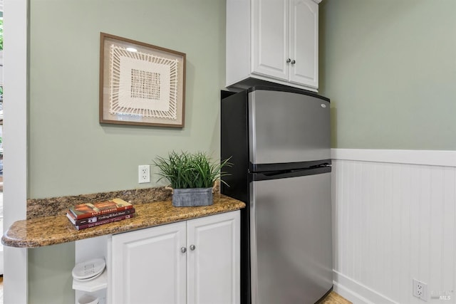 kitchen with freestanding refrigerator, wainscoting, white cabinets, and dark stone countertops
