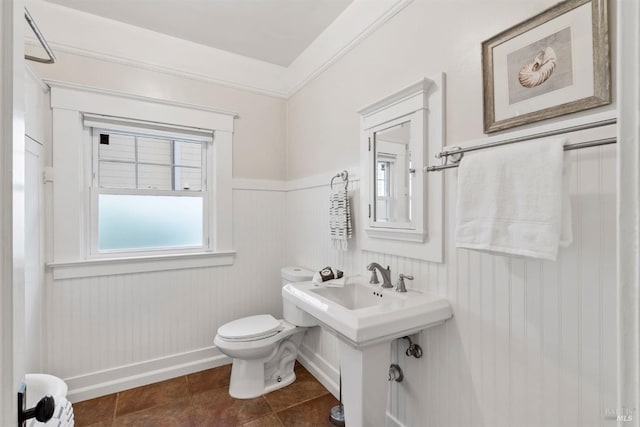 bathroom featuring toilet, tile patterned floors, crown molding, and wainscoting