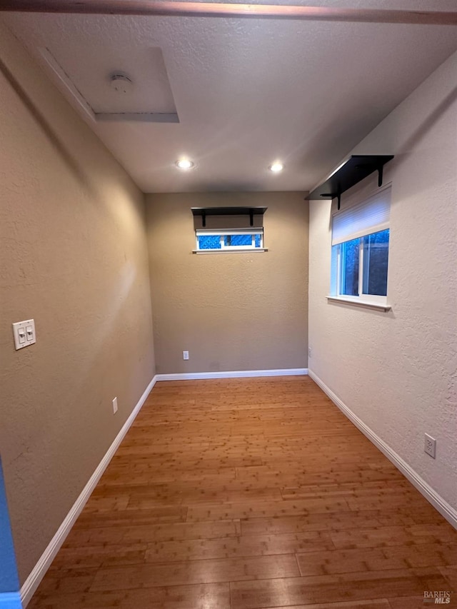 below grade area with recessed lighting, baseboards, wood finished floors, and a textured wall