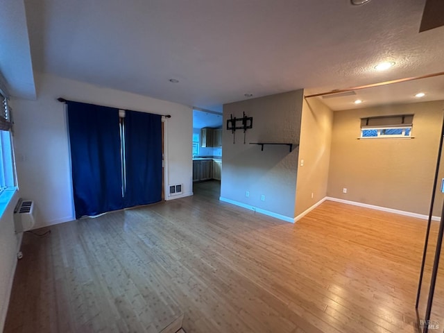 unfurnished living room featuring a wall unit AC, recessed lighting, wood finished floors, visible vents, and baseboards