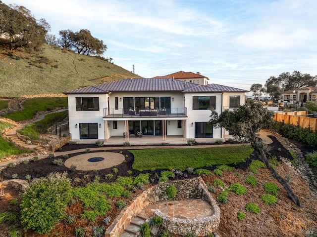 back of property featuring a balcony, metal roof, a standing seam roof, a patio area, and stucco siding