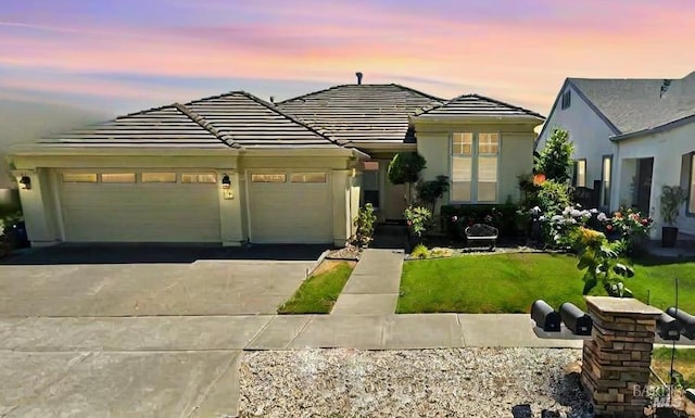 view of front of home featuring driveway, a garage, a lawn, a tile roof, and stucco siding