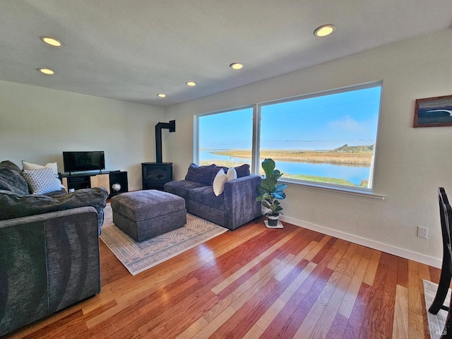 living room with recessed lighting, a water view, wood finished floors, baseboards, and a wood stove