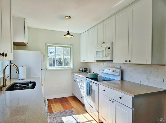 kitchen featuring hanging light fixtures, white appliances, a sink, and white cabinetry