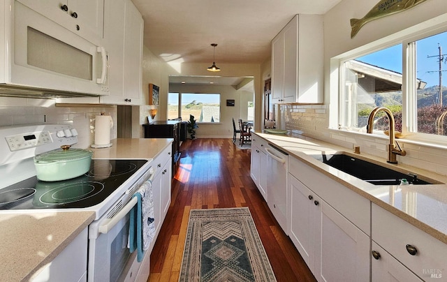 kitchen with white appliances, a sink, white cabinetry, backsplash, and decorative light fixtures