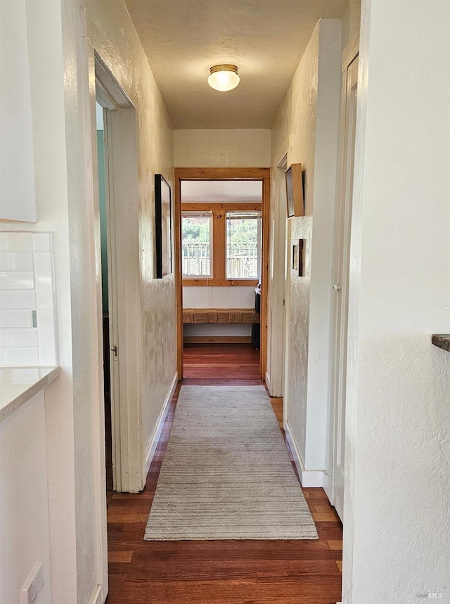 corridor with dark wood-type flooring and a textured wall