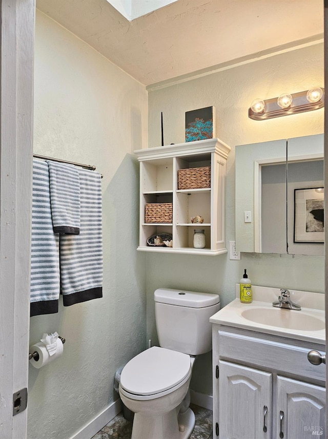 bathroom featuring a skylight, baseboards, a textured wall, toilet, and vanity