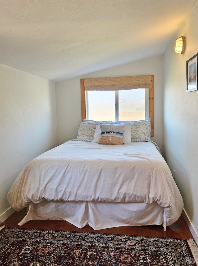 bedroom featuring lofted ceiling, baseboards, and wood finished floors