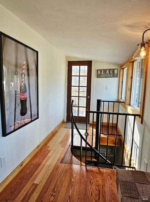 hall with a textured ceiling, baseboards, wood finished floors, and an upstairs landing