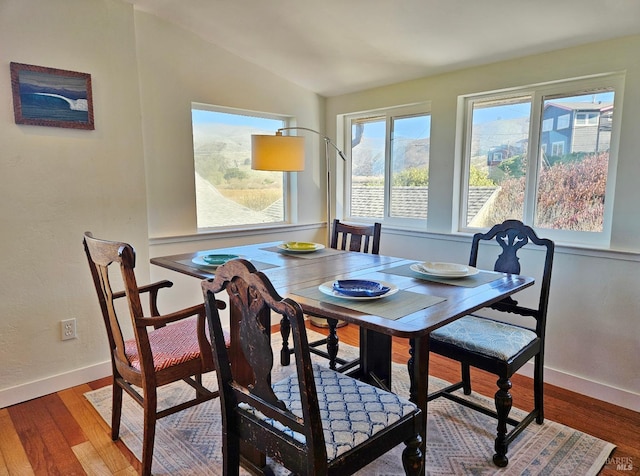 dining space featuring lofted ceiling, wood finished floors, and baseboards