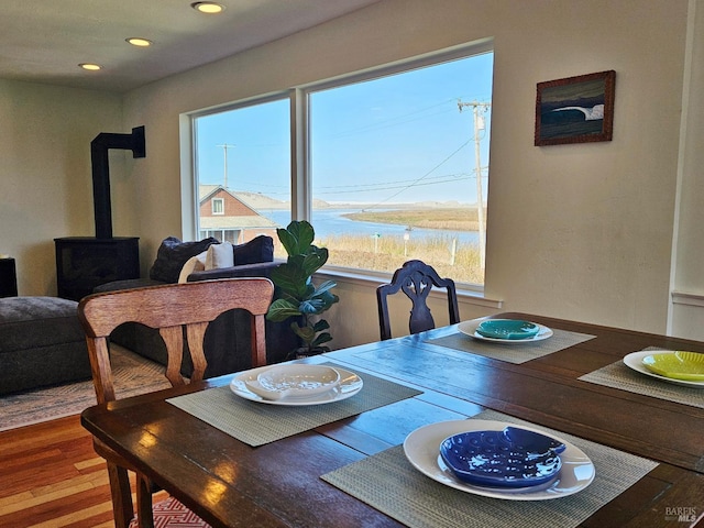 dining room with recessed lighting, a wood stove, a water view, and wood finished floors