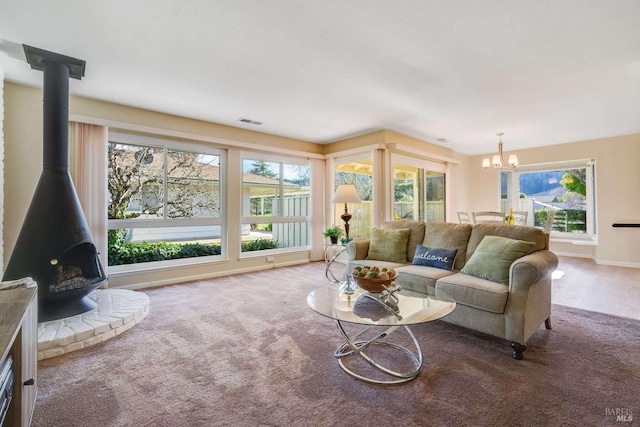 carpeted living room with a wood stove, a notable chandelier, baseboards, and visible vents