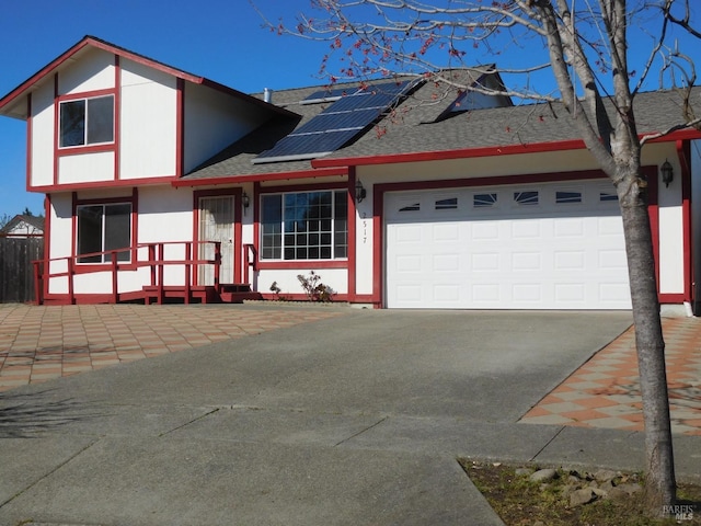 view of front of house featuring a garage, driveway, a shingled roof, roof mounted solar panels, and stucco siding