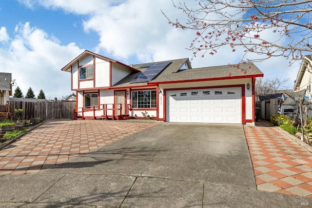 view of front of house featuring a garage, roof mounted solar panels, fence, and driveway