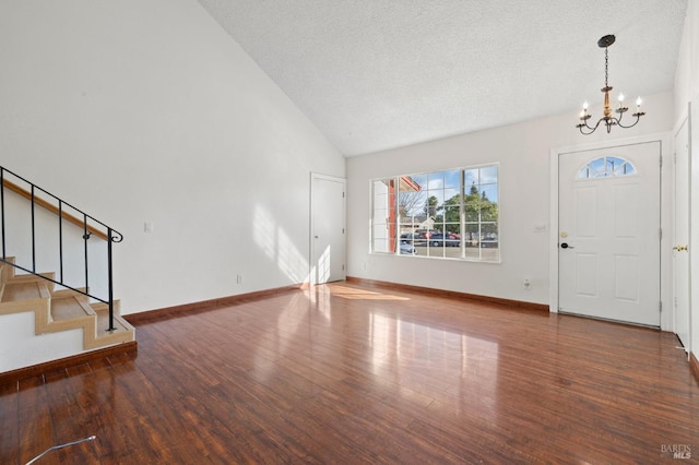 entryway with dark wood-type flooring, vaulted ceiling, a notable chandelier, and stairs