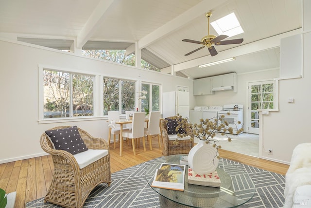 living area featuring light wood finished floors, vaulted ceiling with skylight, baseboards, ceiling fan, and independent washer and dryer