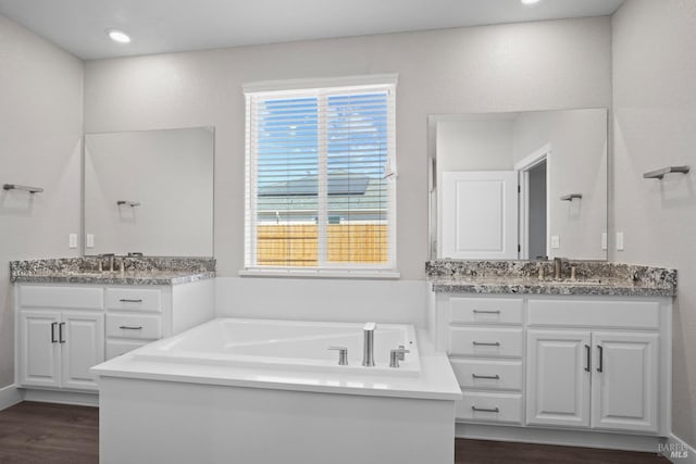 bathroom featuring a garden tub, two vanities, wood finished floors, and a sink