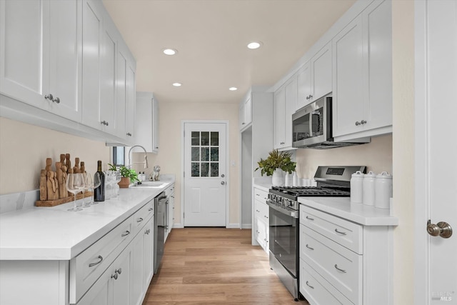 kitchen featuring stainless steel appliances, a sink, white cabinets, light countertops, and light wood-type flooring