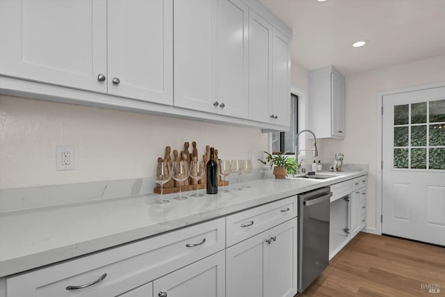 kitchen with light stone counters, light wood finished floors, white cabinets, a sink, and dishwasher