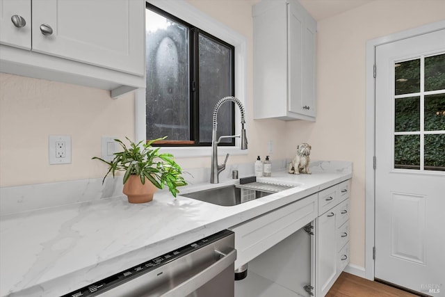 kitchen featuring stainless steel dishwasher, a sink, and white cabinetry