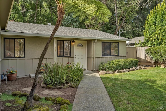 ranch-style house with a shingled roof, fence, board and batten siding, and a front yard