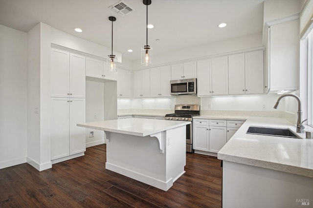 kitchen with stainless steel appliances, light countertops, a sink, and hanging light fixtures