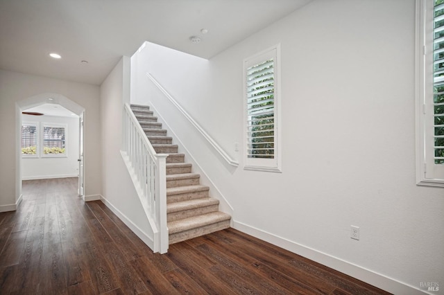 staircase with baseboards, arched walkways, wood finished floors, and recessed lighting