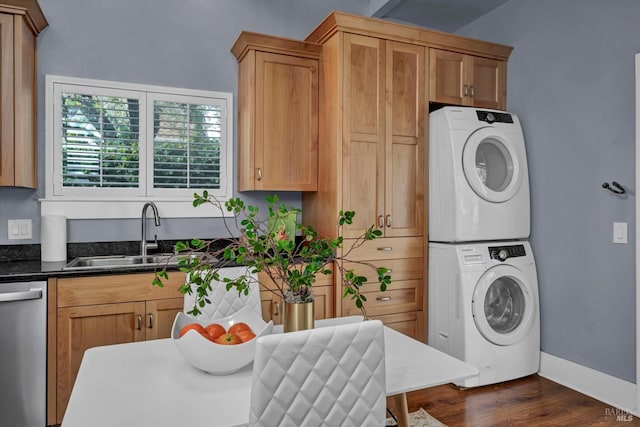 laundry area with stacked washer and dryer, laundry area, a sink, baseboards, and dark wood finished floors