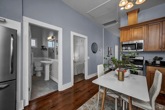 kitchen with dark wood finished floors, dark countertops, appliances with stainless steel finishes, brown cabinetry, and baseboards