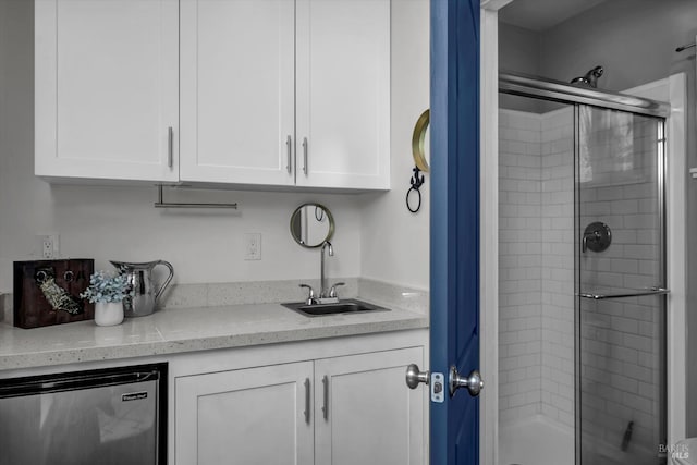 interior space with white cabinets, a sink, stainless steel refrigerator, and light stone countertops