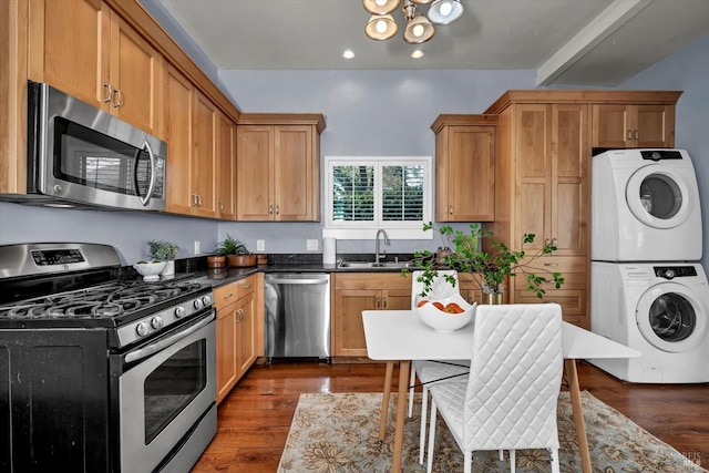 kitchen with a sink, appliances with stainless steel finishes, dark wood finished floors, and stacked washer / dryer