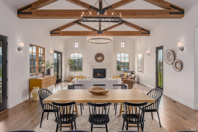 dining room with a chandelier, high vaulted ceiling, a large fireplace, a healthy amount of sunlight, and light wood-style floors