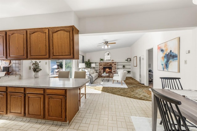 kitchen with brown cabinets, lofted ceiling, light countertops, a brick fireplace, and ceiling fan