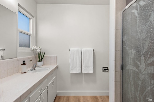 full bath featuring wood finished floors, vanity, baseboards, backsplash, and a shower stall