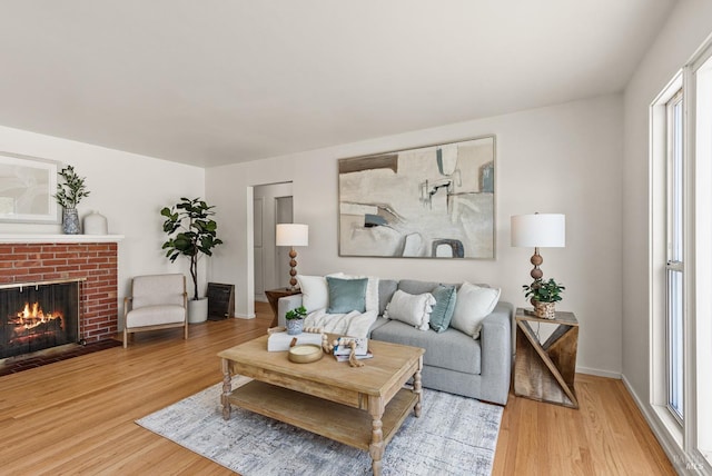 living area with a brick fireplace, light wood-style flooring, and baseboards