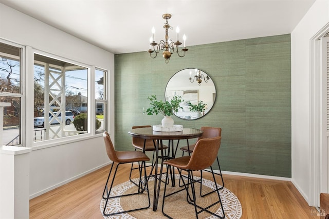 dining space featuring an accent wall, a chandelier, light wood-type flooring, baseboards, and wallpapered walls